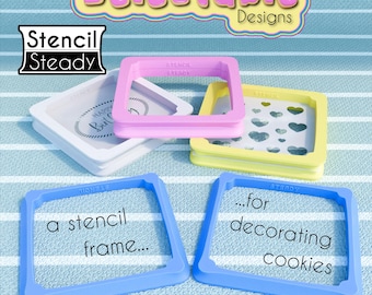 May include: Four different colored plastic cookie stencils. The stencils are square shaped and have different designs. The stencils are for decorating cookies. The text "Delectable Designs" is at the top of the image. The text "Stencil Steady" is in the top left corner of the image.