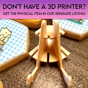 May include: A beige 3D printed stand for displaying cookies or other small items. The stand has a triangular base and two vertical supports that meet at the top. The stand is designed to hold items securely in place.