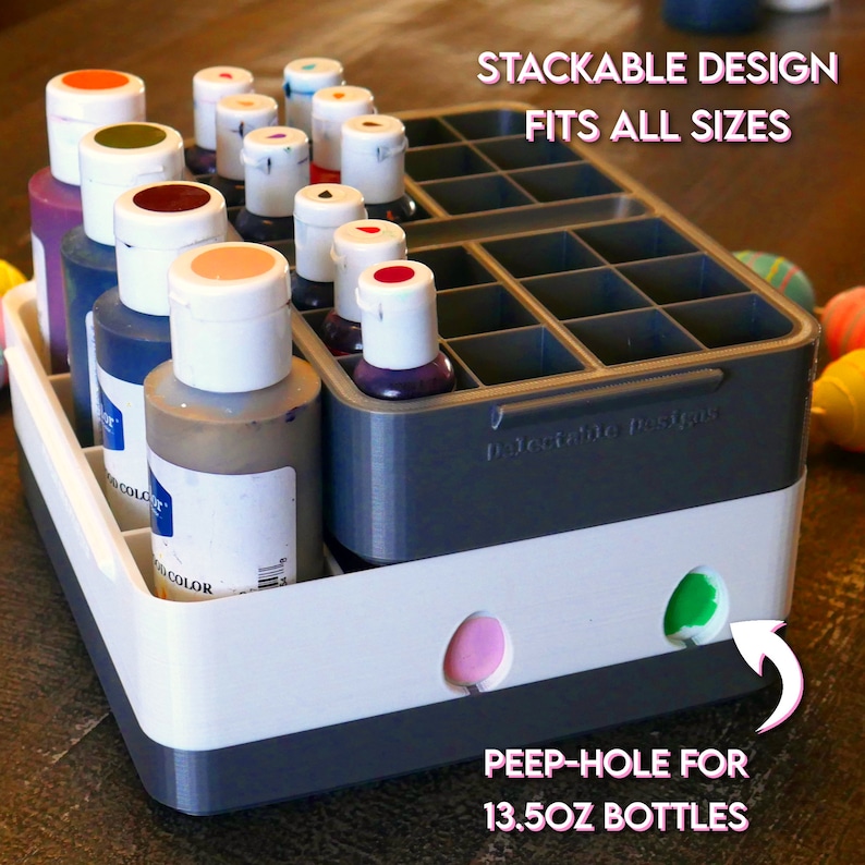May include: A gray and white plastic organizer with multiple compartments for storing bottles of food coloring. The organizer has a label that reads "Stackable Design Fits All Sizes". The bottom of the organizer has two holes for larger bottles.