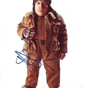 May include: A man wearing a brown leather jacket with a fur collar and a brown leather aviator hat. He is wearing brown pants and brown leather boots. He is holding a small, silver object in his right hand.