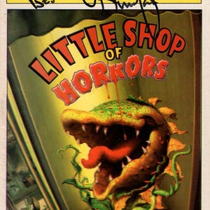 May include: Playbill cover for "Little Shop of Horrors" at the Virginia Theatre. The cover shows a large, menacing plant with a red tongue and dripping red liquid. The Playbill is signed and includes the text "All the Best!"