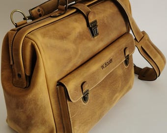 May include: A tan leather satchel with a top handle, shoulder strap, and front pocket. The bag features metal clasps and hardware. The text "W. Bauer" is visible on the front pocket. The bag has a vintage, worn appearance.