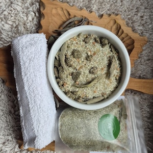Peut inclure: Un bol blanc rempli d'un mélange de sel de bain vert et blanc, une serviette blanche et un sac en plastique transparent avec un mélange de sel de bain vert et blanc. Les sels de bain sont sur une surface en bois.