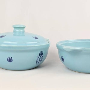 May include: A light blue ceramic casserole dish with a lid, both featuring a blue floral design. The dish has a rounded shape and a slightly flared rim.