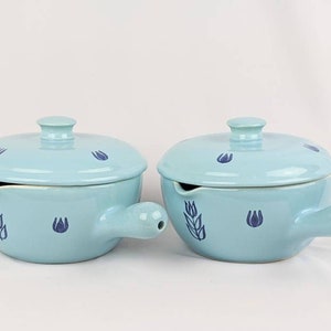 May include: Two light blue ceramic sauce pots with lids and handles. Each pot has a blue wheat design and blue flower accents.