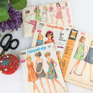 May include: Four vintage sewing patterns for dresses. The patterns are from Simplicity and McCall's. The patterns feature different styles of dresses, including a maternity dress, a 'how to sew' pattern, and a dress with a floral print.