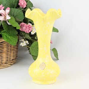 May include: A yellow ceramic vase with a ruffled top and a white speckled design. The vase is about 7 inches tall.