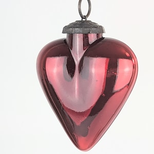 May include: A red glass heart ornament with a metal loop and cap. The ornament is shiny and reflects light.