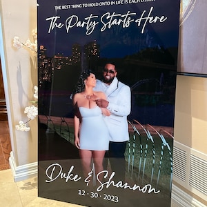 Peut inclure: Une pancarte de bienvenue de mariage avec un fond noir et du texte blanc. Le texte indique "La meilleure chose à laquelle s'accrocher dans la vie, c'est l'un l'autre. La fête commence ici. Duke & Shannon 12.30.2023". Une photo d'un couple est en arrière-plan.
