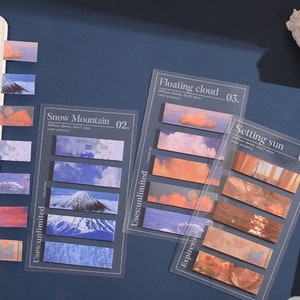 May include: Set of six colorful, illustrated, adhesive note tabs with the text "Floating cloud 03.", "Setting sun 04.", and "Snow Mountain 02."  The tabs are designed to be used as bookmarks or to mark pages in a notebook.