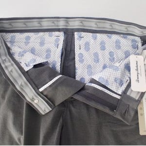 K&ouml;nnte beinhalten: Dunkelgraue Hose mit einem Bund, der ein wiederkehrendes Marlin-Logo-Muster aufweist. Das Innenfutter zeigt einen hellblauen Ananasdruck auf wei&szlig;em Grund. Die angebrachten Etiketten enthalten den Markennamen Tommy Bahama und den Text Sun Shelter.