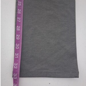 K&ouml;nnte beinhalten: Ein graues Stoffhosenbein mit feiner horizontaler Rippenstruktur und einem gen&auml;hten Saum. Ein violettes Ma&szlig;band ist vertikal an der Seite angebracht und zeigt eine L&auml;ngenmessung, die von 58 cm bis 89 cm reicht.
