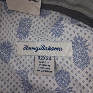 K&ouml;nnte beinhalten: Eine Hose mit wei&szlig;em Innenfutter, das mit einem blauen Ananas- und Rautenmuster bedruckt ist. Ein Tommy Bahama Markenschild ist befestigt. Das Gr&ouml;&szlig;enetikett zeigt 32x34 und gibt an, dass das Kleidungsst&uuml;ck in Vietnam hergestellt wurde. Der Bund ist grau.