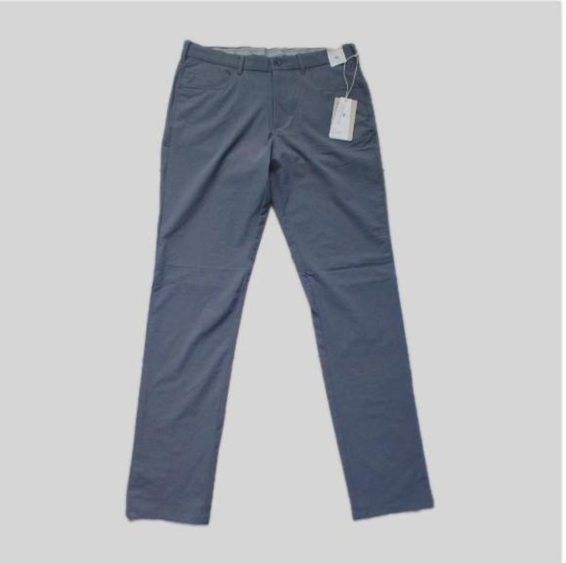 K&ouml;nnte beinhalten: Eine schieferblaue Hose mit einem Standardbund mit G&uuml;rtelschlaufen, einem Knopf- und Rei&szlig;verschluss sowie zwei Vordertaschen. Ein wei&szlig;es, rechteckiges Produktetikett ist mit einer d&uuml;nnen wei&szlig;en Schnur am Bund befestigt.
