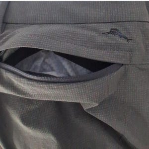 K&ouml;nnte beinhalten: Dunkelolivgr&uuml;ne Hose mit strukturiertem Gittermuster und einer Rei&szlig;verschlusstasche. Ein kleines, schwarz gesticktes Marlin-Fisch-Logo befindet sich &uuml;ber der Taschen&ouml;ffnung, die einen Blick auf ein helles Innenfutter freigibt.