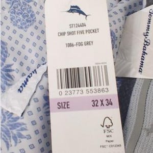 K&ouml;nnte beinhalten: Eine graue Hose mit wei&szlig;em Innenfutter, das mit einem blauen Ananas- und Rautenmuster bedruckt ist. Ein wei&szlig;es Produktetikett ist befestigt, das den Text Tommy Bahama, Chip Shot Five Pocket, 1086-Fog Grey und die Gr&ouml;&szlig;e 32 x 34 zeigt.