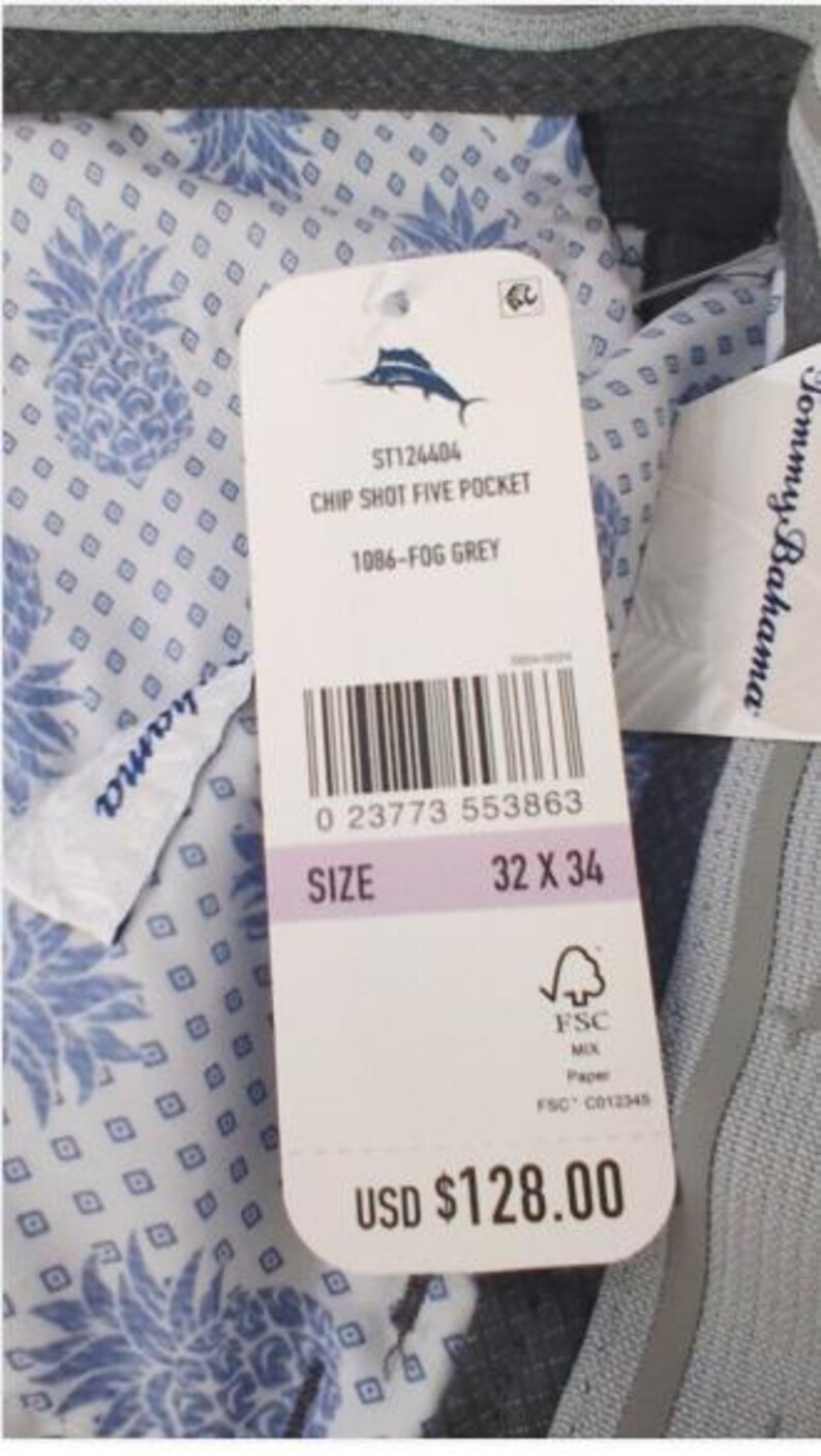K&ouml;nnte beinhalten: Eine graue Hose mit wei&szlig;em Innenfutter, das mit einem blauen Ananas- und Rautenmuster bedruckt ist. Ein wei&szlig;es Produktetikett ist befestigt, das den Text Tommy Bahama, Chip Shot Five Pocket, 1086-Fog Grey und die Gr&ouml;&szlig;e 32 x 34 zeigt.