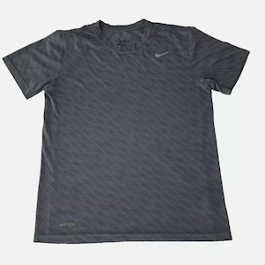 Puede incluir: Una camiseta gris de manga corta con un patrón diagonal y un logotipo de Nike en el pecho izquierdo. La camiseta tiene el texto "Dri-FIT" en la etiqueta.