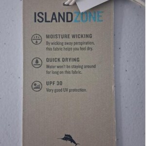 K&ouml;nnte beinhalten: Ein rechteckiges beiges Kleidungsetikett mit einer wei&szlig;en Schnur. Der Text lautet ISLANDZONE, MOISTURE WICKING, QUICK DRYING und UPF 30. Es enth&auml;lt Symbole f&uuml;r jede Funktion, eine kleine schwarze Marlin-Grafik und die Website TOMMYBAHAMA.COM.