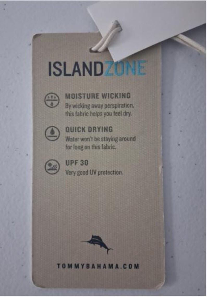 K&ouml;nnte beinhalten: Ein rechteckiges beiges Kleidungsetikett mit einer wei&szlig;en Schnur. Der Text lautet ISLANDZONE, MOISTURE WICKING, QUICK DRYING und UPF 30. Es enth&auml;lt Symbole f&uuml;r jede Funktion, eine kleine schwarze Marlin-Grafik und die Website TOMMYBAHAMA.COM.