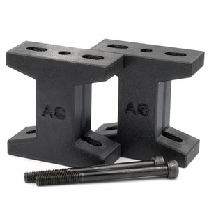 Könnte beinhalten: Zwei schwarze T-förmige Kunststoff-Erhöhungen mit den Buchstaben "AO" auf der Vorderseite. Zwei schwarze Schrauben sind im Lieferumfang enthalten.