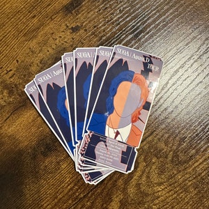 May include: A stack of six blue, white, and red ticket-shaped stickers with the text "SUGA Agust D TOUR" and a stylized illustration of a person with blue and red hair. The text "DAY The Final LIVE STREAMING August 6, 2023 Sunday 5:00 PM (KST) KSPO DOME Seoul, Korea" is printed on the bottom sticker.