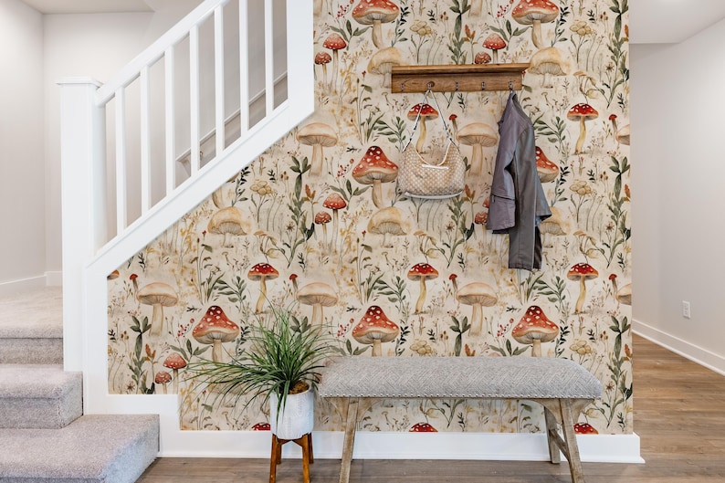 Puede incluir: Papel pintado con un patr&oacute;n bot&aacute;nico repetitivo de varios hongos, flores silvestres y follaje en tonos rojos, marrones y verdes sobre un fondo beige claro, aplicado en una pared junto a una escalera con un perchero y un banco.