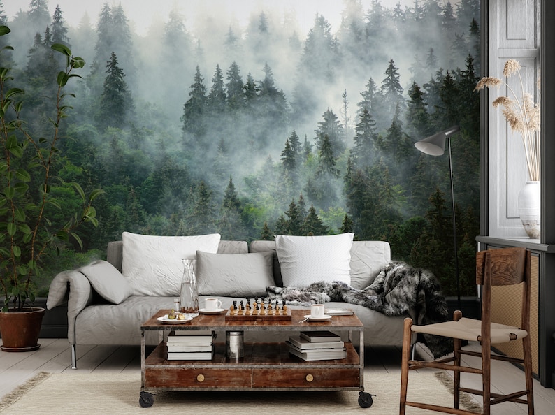 May include: A living room with a forest mural on the wall. A gray sofa with white pillows and a faux fur throw is in front of the mural. A wooden coffee table with a chess set and books sits in front of the sofa.