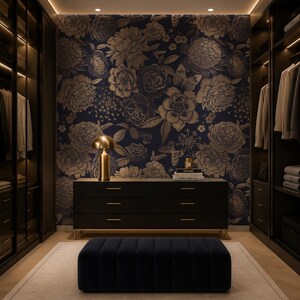 May include: A walk-in closet featuring dark wood cabinetry with integrated lighting, a central black dresser with gold hardware, a navy blue velvet ottoman, and a dark blue wallpaper backdrop with a gold floral and butterfly pattern.