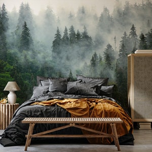 May include: A bedroom scene featuring a forest mural, a bed with dark gray bedding and an orange throw blanket. A wooden bench sits at the foot of the bed. A wooden side table with a lamp and a woven cabinet complete the room's decor.