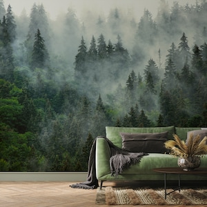 May include: A forest-themed wall mural featuring a dense, green coniferous forest shrouded in mist. The mural creates a serene atmosphere. A green sofa with throw pillows and a decorative vase with dried plants are in front of the mural.