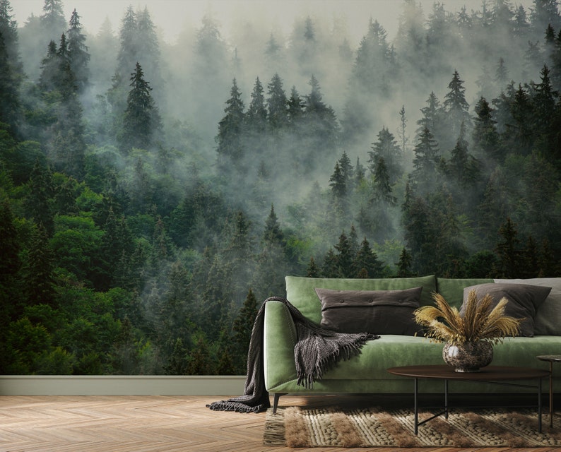 May include: A forest-themed wall mural featuring a dense, green coniferous forest shrouded in mist. The mural creates a serene atmosphere. A green sofa with throw pillows and a decorative vase with dried plants are in front of the mural.