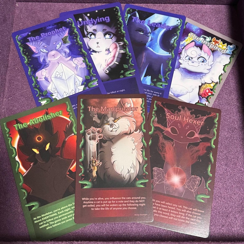 Puede incluir: Un conjunto de cartas coleccionables de fantas&iacute;a con gatos antropom&oacute;rficos. Cada carta tiene una ilustraci&oacute;n y un t&iacute;tulo &uacute;nicos, como "The Prophet" y "The Manipulator". Las cartas est&aacute;n sobre un fondo morado.
