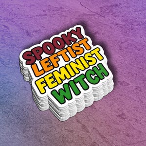 May include: A stack of stickers with the words "Spooky Leftist Feminist Witch" in a rainbow color scheme. The stickers are on a purple background.
