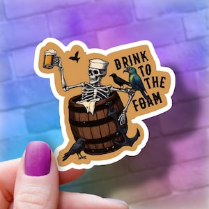 May include: A sticker featuring a skeleton pirate holding a beer mug and sitting in a barrel. The pirate is wearing a captain's hat and has a parrot and two crows perched on his shoulders. The sticker says "Drink to the Foam".