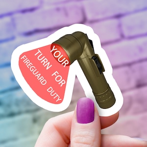 May include: A sticker of a gold flashlight with a red beam shining on the words "YOUR TURN FOR FIREGUARD DUTY".