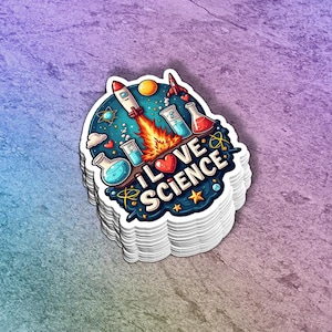 May include: A stack of white stickers with a colorful design. The sticker features a rocket ship launching, beakers, and the words "I LOVE SCIENCE" in white and red. The background is a gradient of blue, purple, and pink.