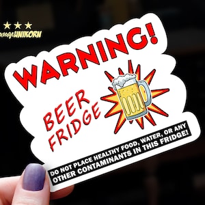 May include: A white sticker with the text "WARNING! BEER FRIDGE" in red and black. It features a cartoon beer mug with a yellow explosion graphic. The bottom text reads "DO NOT PLACE HEALTHY FOOD, WATER, OR ANY OTHER CONTAMINANTS IN THIS FRIDGE!"