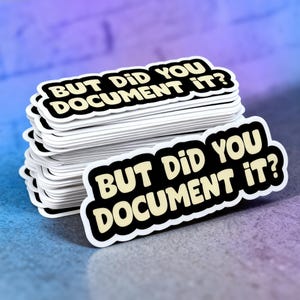 May include: A stack of white stickers with the text "BUT DID YOU DOCUMENT IT?" in a black and white design. The stickers are stacked on a blue and purple gradient surface.