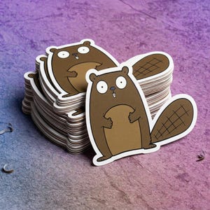 May include: A stack of die-cut stickers featuring a cartoon beaver with wide, surprised eyes, a brown body, a lighter tan belly, and a dark brown tail with a cross-hatched pattern. The beaver has two small white teeth visible in its mouth.