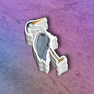 May include: A blue and gray heron sticker with a long, thin beak and long legs. The sticker is on a purple and blue background.