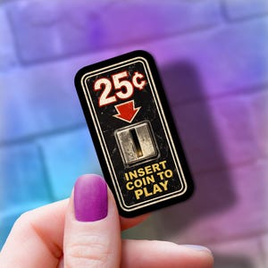 May include: A vintage-style black and white sign with the text "25¢" and "INSERT COIN TO PLAY". The sign has a red arrow and a coin slot. The sign is rectangular and has a white border.