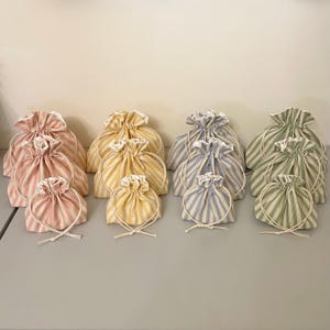 May include: A set of 10 striped fabric drawstring bags in various sizes. The bags are in shades of blue, yellow, and pink.