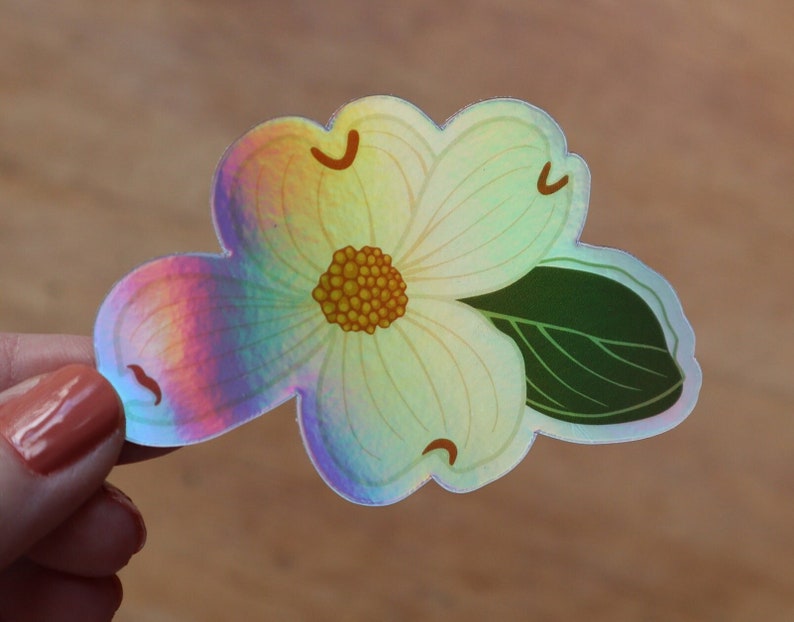 May include: A holographic sticker of a white flower with a yellow center and a green leaf. The flower has a rainbow iridescent finish.