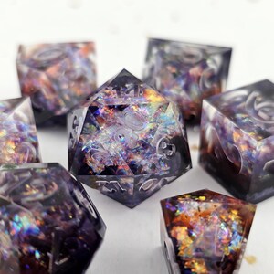 May include: A set of polyhedral dice with a shimmering, iridescent interior. The dice are clear with a dark purple and gold glitter effect. The dice are in various shapes, including a twenty-sided die and several six-sided dice.