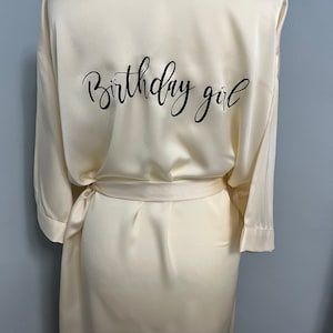 May include: A white satin robe with the text "Birthday girl" embroidered on the back.