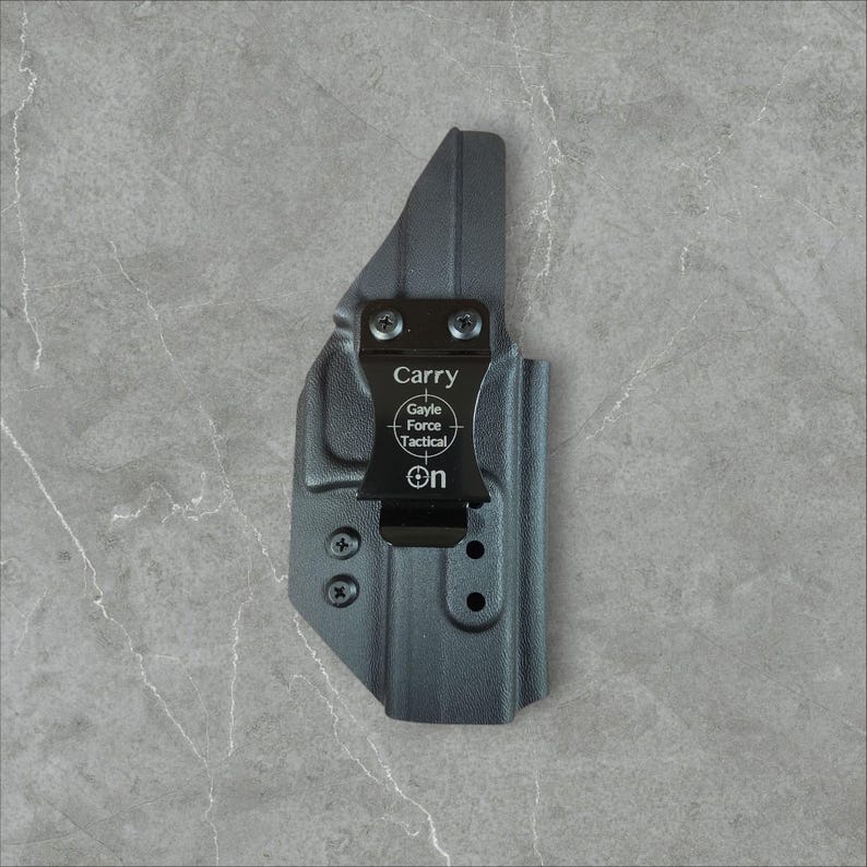 K&ouml;nnte beinhalten: Eine schwarze Holster mit einem Metallclip. Auf dem Clip steht oben das Wort "Carry", darunter "Gayle Force Tactical" und "ON". Die Holster ist f&uuml;r das Tragen am K&ouml;rper konzipiert.