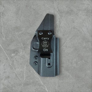 May include: A black holster with a clip, featuring the text "Carry" and "On." The holster has the "Gayle Force Tactical" logo. The holster is made of a durable material and is designed to hold a firearm.