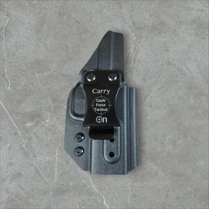 May include: A gray Gayle Force Tactical carry holster. The holster has a black clip with the word "Carry" and the Gayle Force Tactical logo. The word "On" is printed on the clip. The holster is made of a durable material.