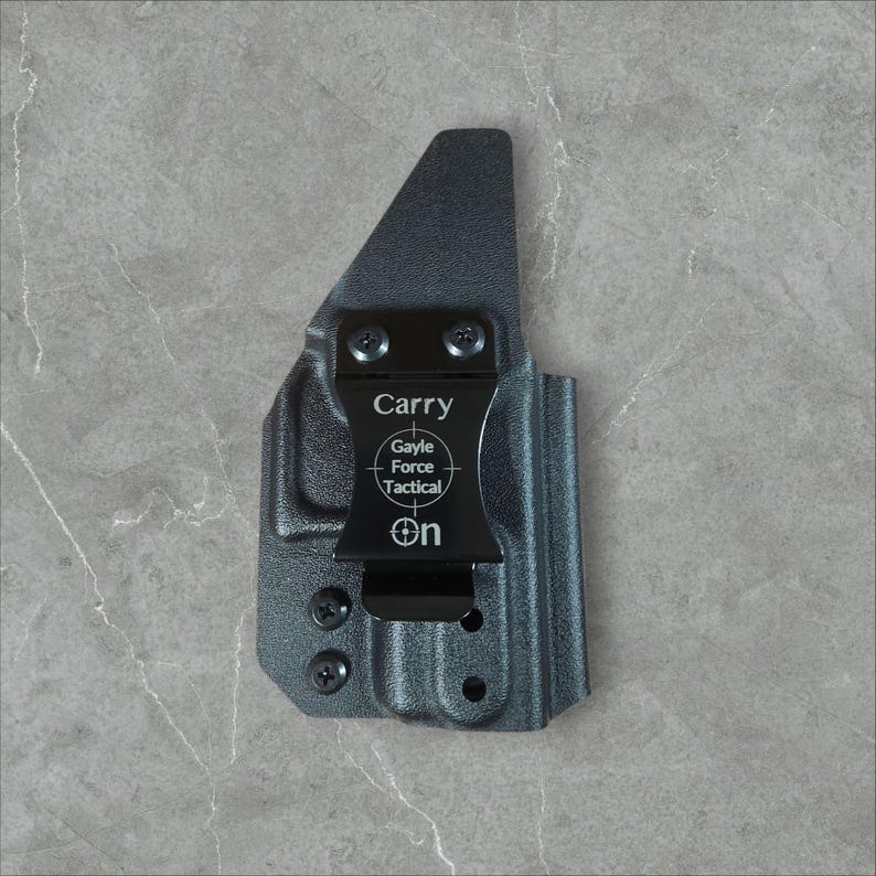 K&ouml;nnte beinhalten: Eine schwarze Holster mit einem Metallclip. Auf der Holster stehen die W&ouml;rter "Carry" und "Gayle Force Tactical". Die Holster ist zum Tragen am K&ouml;rper konzipiert.